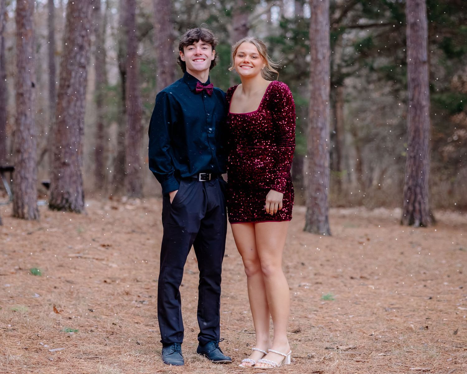 A couple poses together in a pine forest wearing formal attire during a photo session.