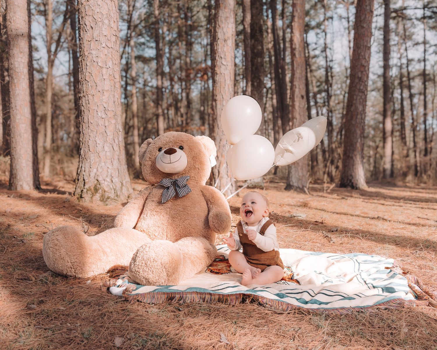 A large teddy bear sits in a wooded forest setting with a book and blanket for a cozy reading scene.