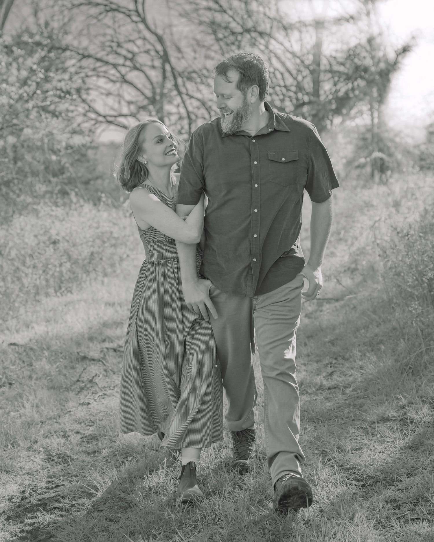 Black and white photo of a laughing couple walking together on a nature path.