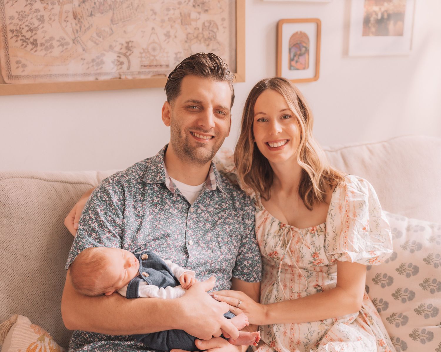 Happy couple sits on a couch smiling while holding their newborn baby.