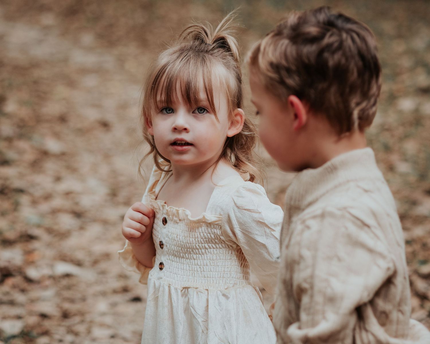 Two young children in vintage-style clothing share tender moments while playing together in autumn leaves.
