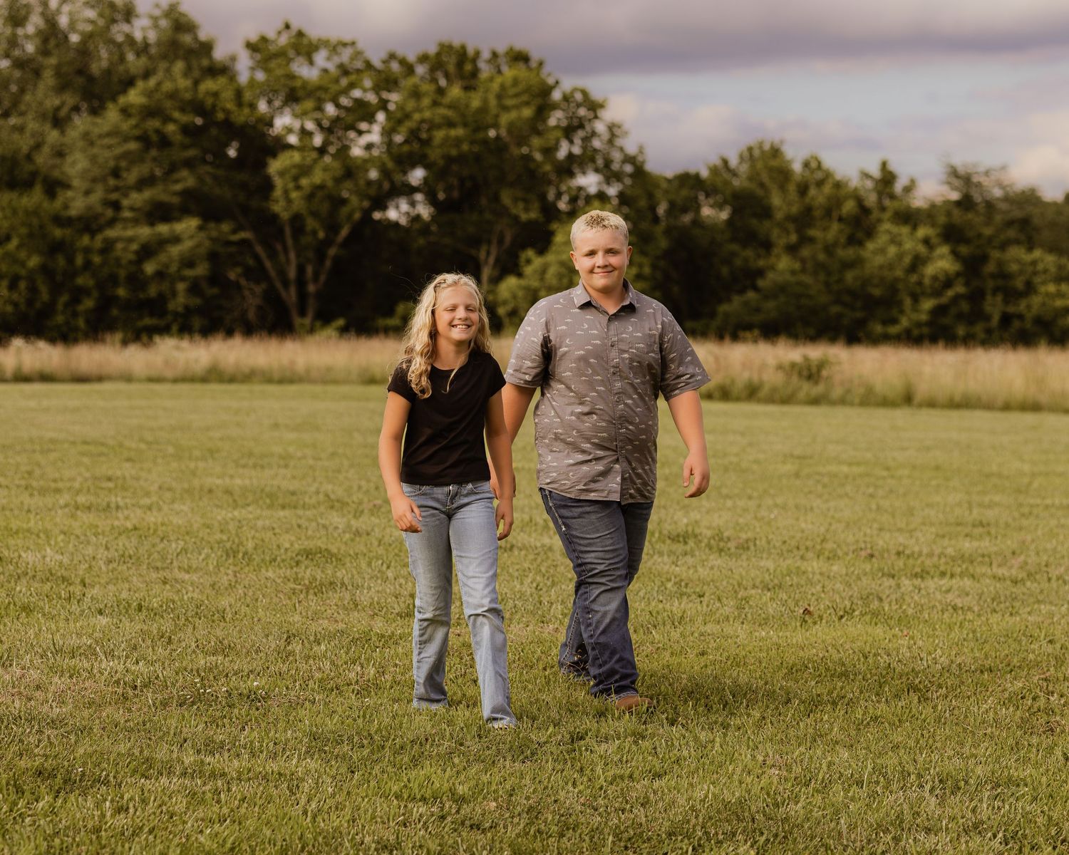 Smiling couple holding hands and walking through a lush green field on a partly cloudy day.