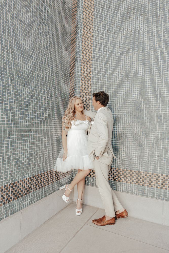 A couple poses together against a blue tiled wall in a series of intimate photos.