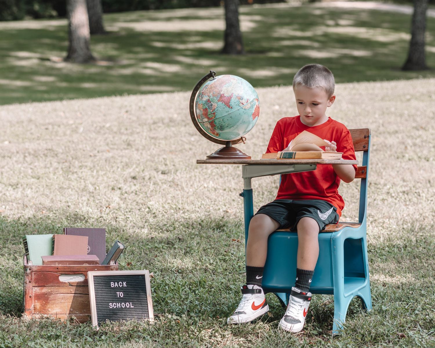 Back to school photo setup with vintage blue desk, globe, and letterboard in an outdoor setting.