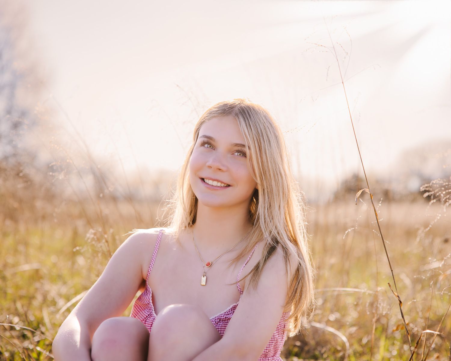 Young blonde girl sitting in a sunny meadow smiling with tall grass around.
