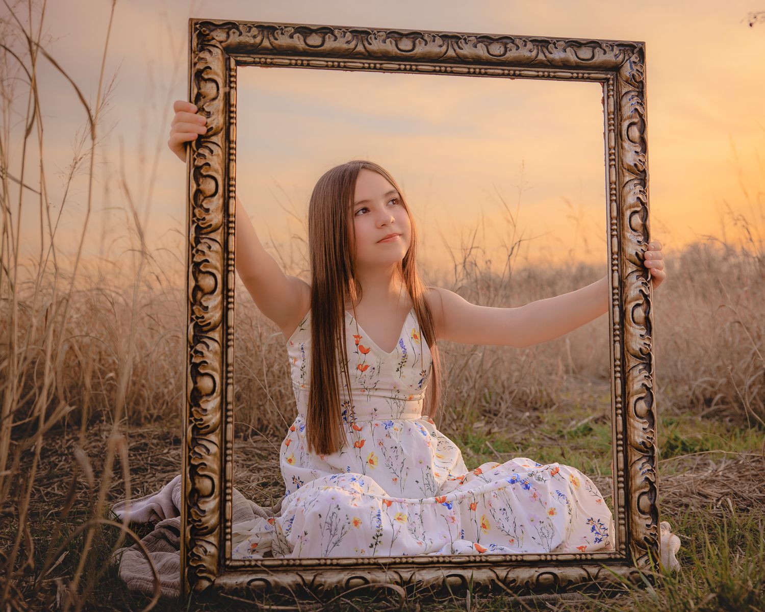 A rustic wooden frame captures a dreamy sunset portrait session in a golden field of tall grass.