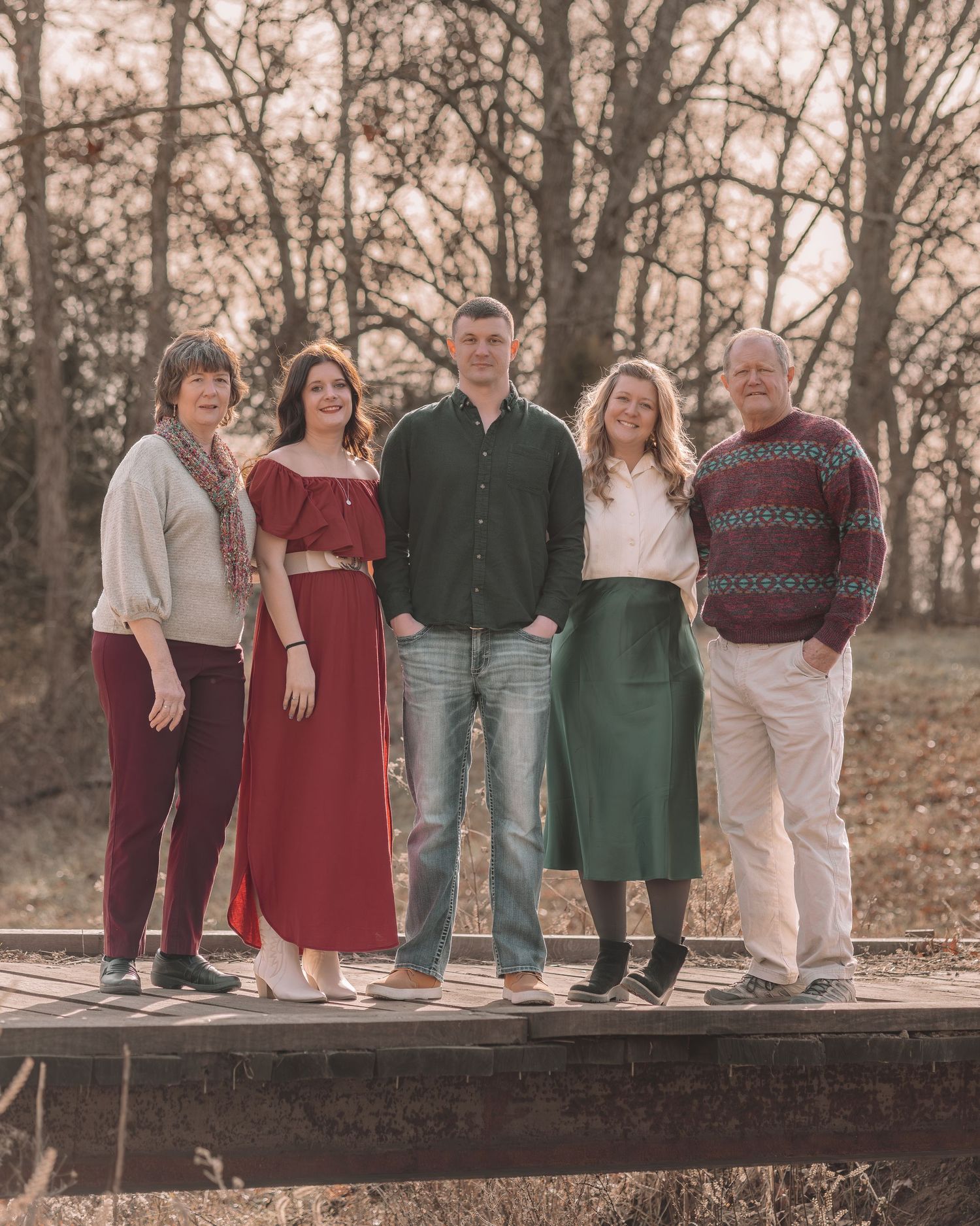 A family group poses together on a wooden platform in autumn, wearing coordinated burgundy, green and neutral tones.