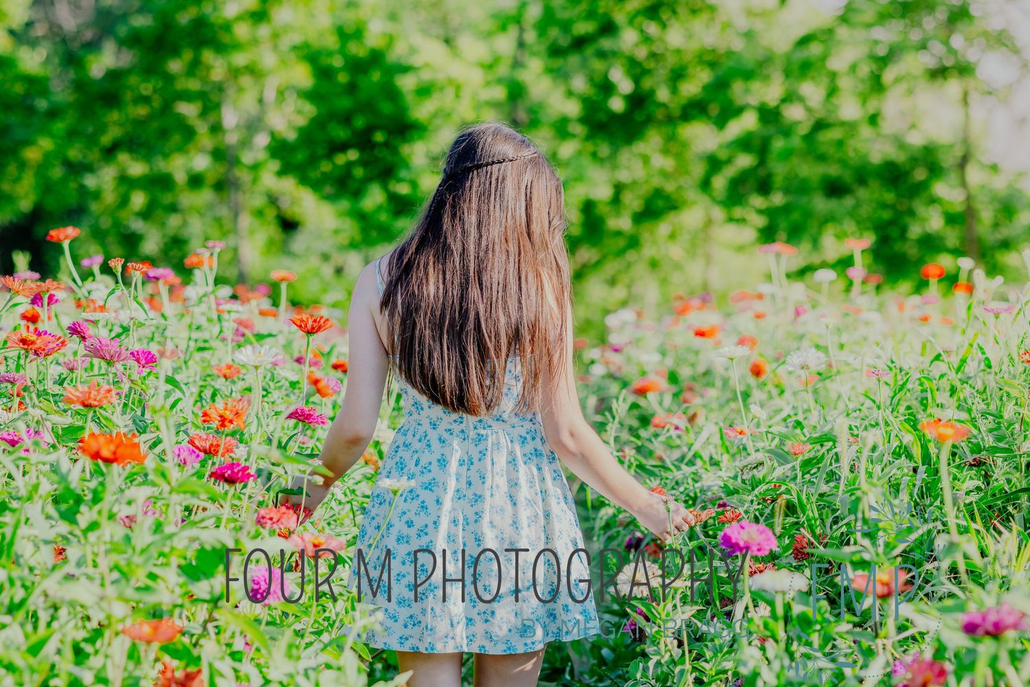 Someone with long brown hair walks through a vibrant wildflower meadow filled with red and pink blooms on a sunny day.