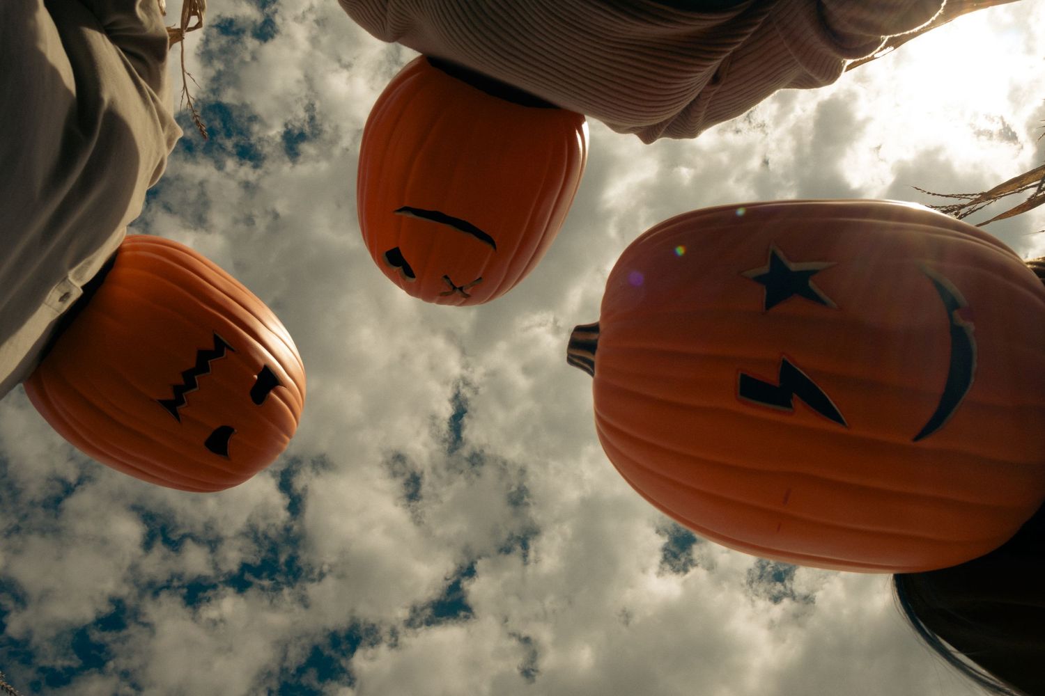 Looking up at carved Halloween pumpkins hanging from tree branches against a cloudy sky.