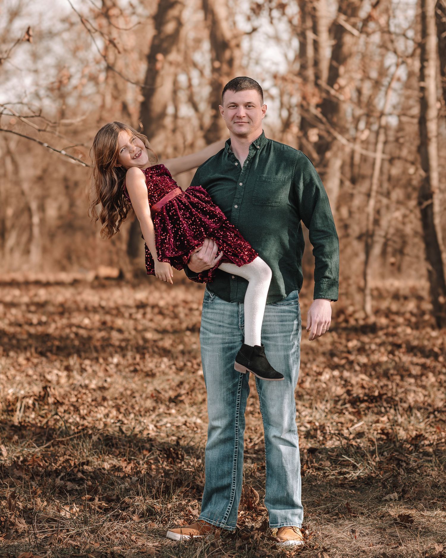 A couple shares a playful moment together in a wooded area with fallen autumn leaves.