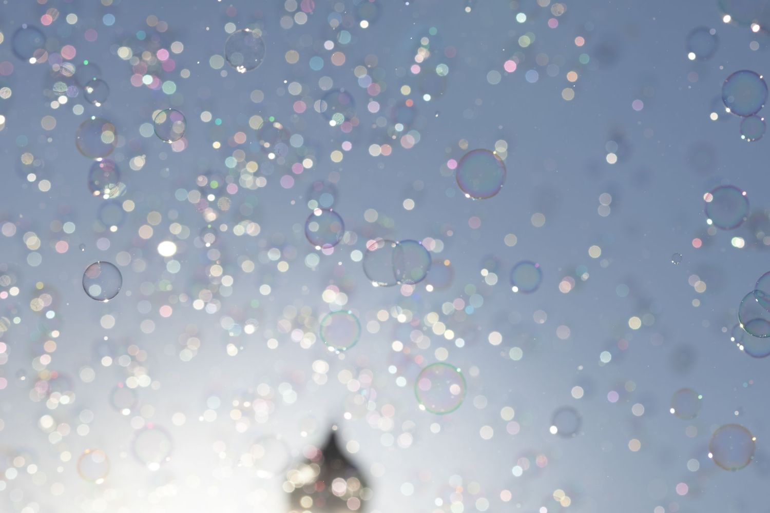 Colorful soap bubbles floating against a bright blue sky with sunlight creating a magical ethereal effect.