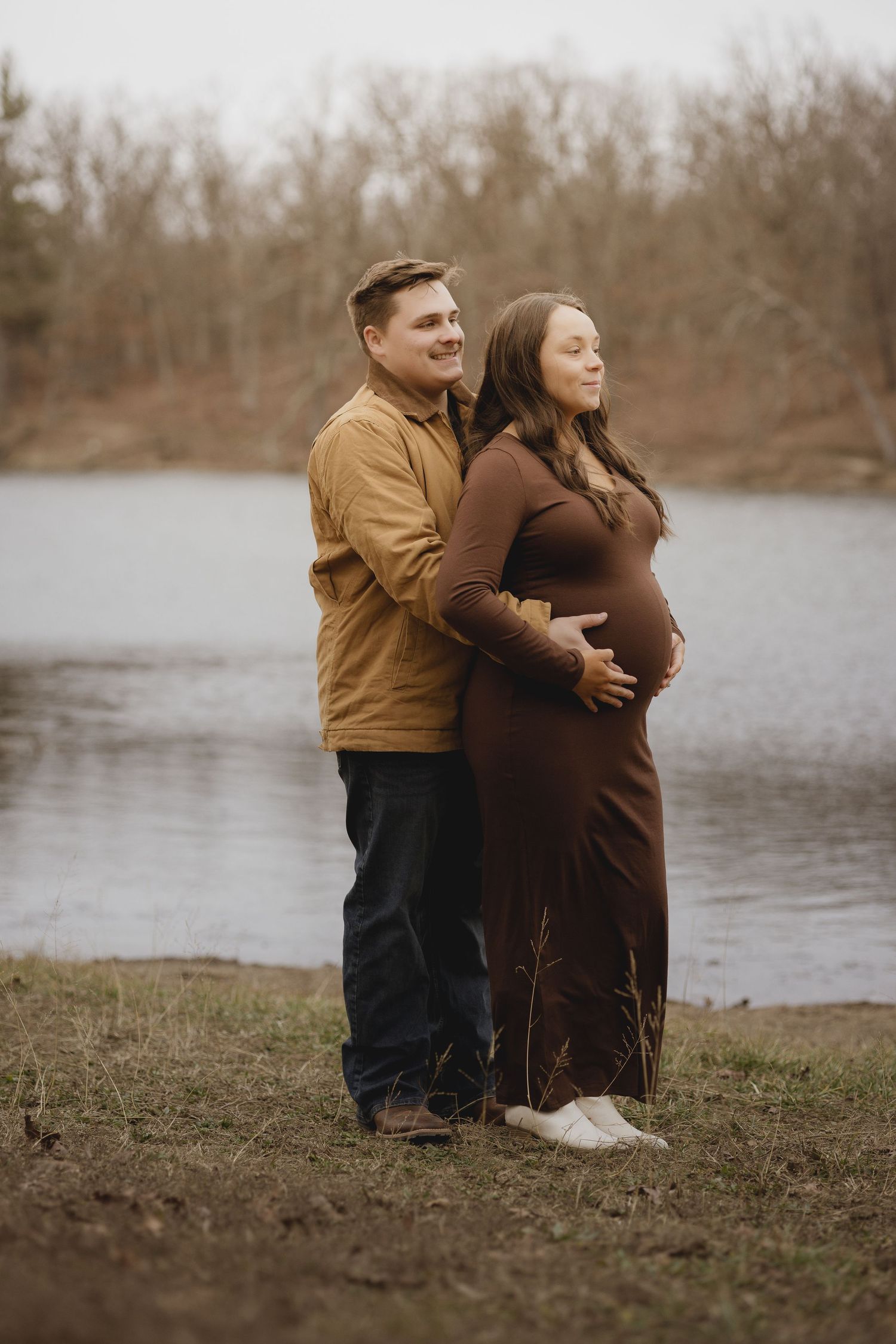 A couple shares intimate moments by a serene lake on an overcast day.