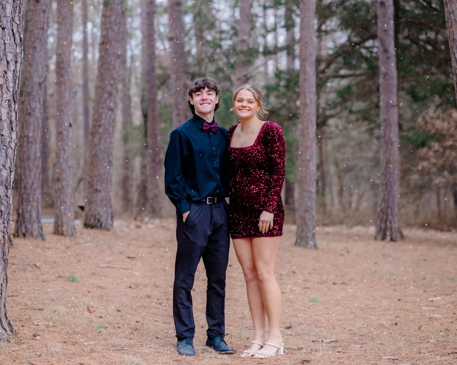 Friends pose playfully in a pine forest with fallen needles covering the ground during a photo session.