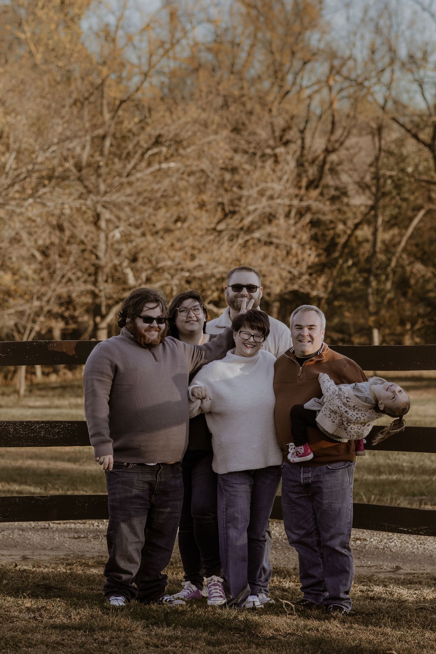 A family group poses playfully in casual attire on grass during a warm autumn day photoshoot.