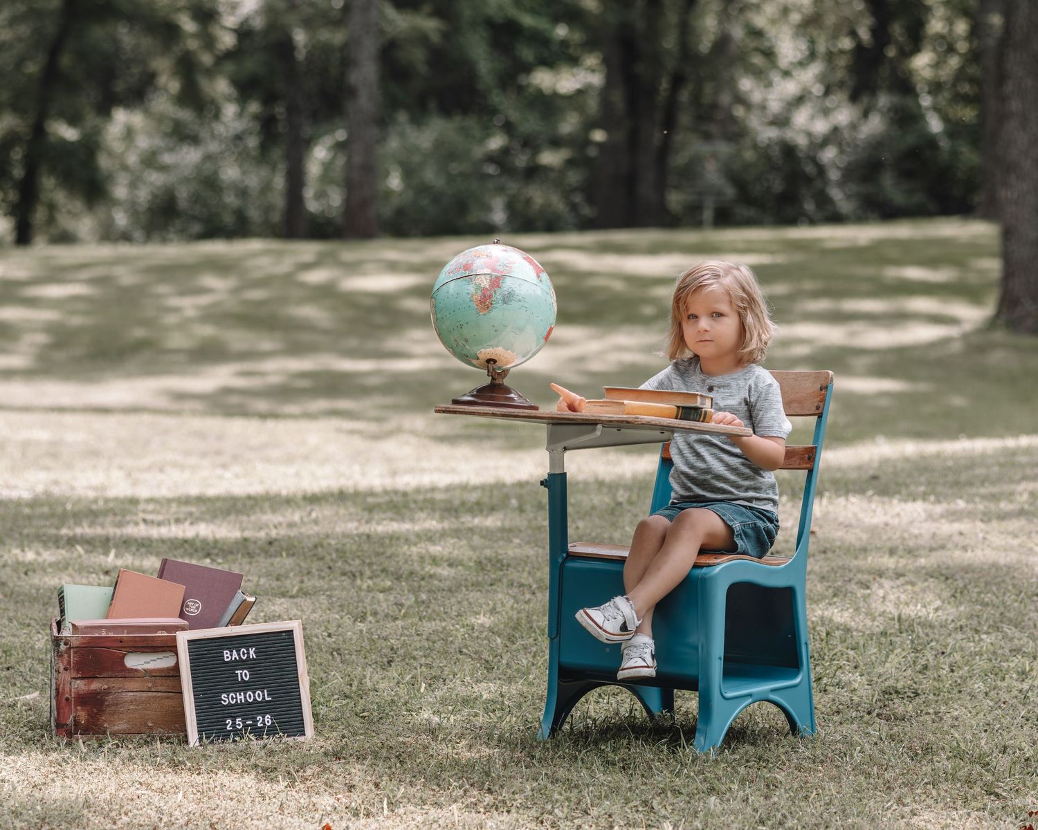 A creative back-to-school photo session featuring a teal desk and vintage props on a sunny lawn.