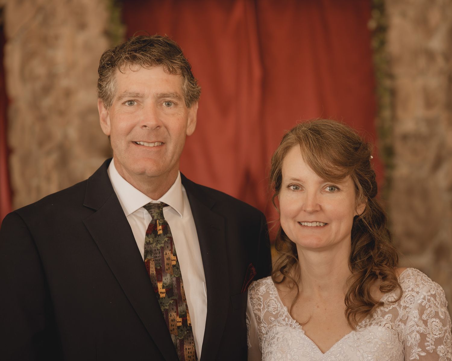 Formal portrait series of wedding couple in front of rustic stone wall with red drapery.