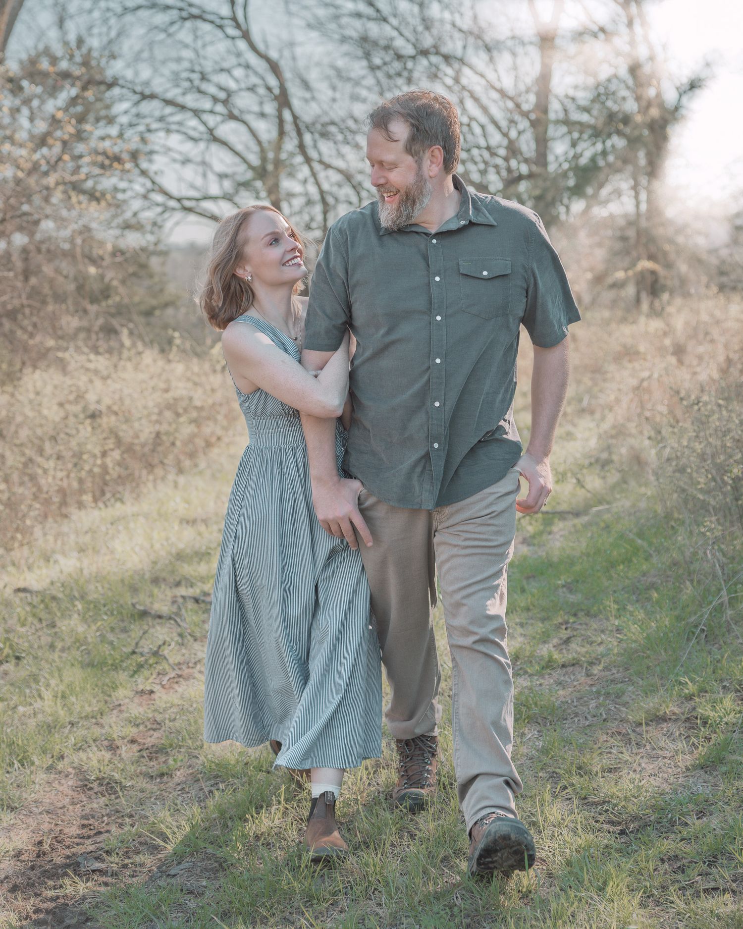 Happy couple walking and laughing together on a grassy outdoor trail.