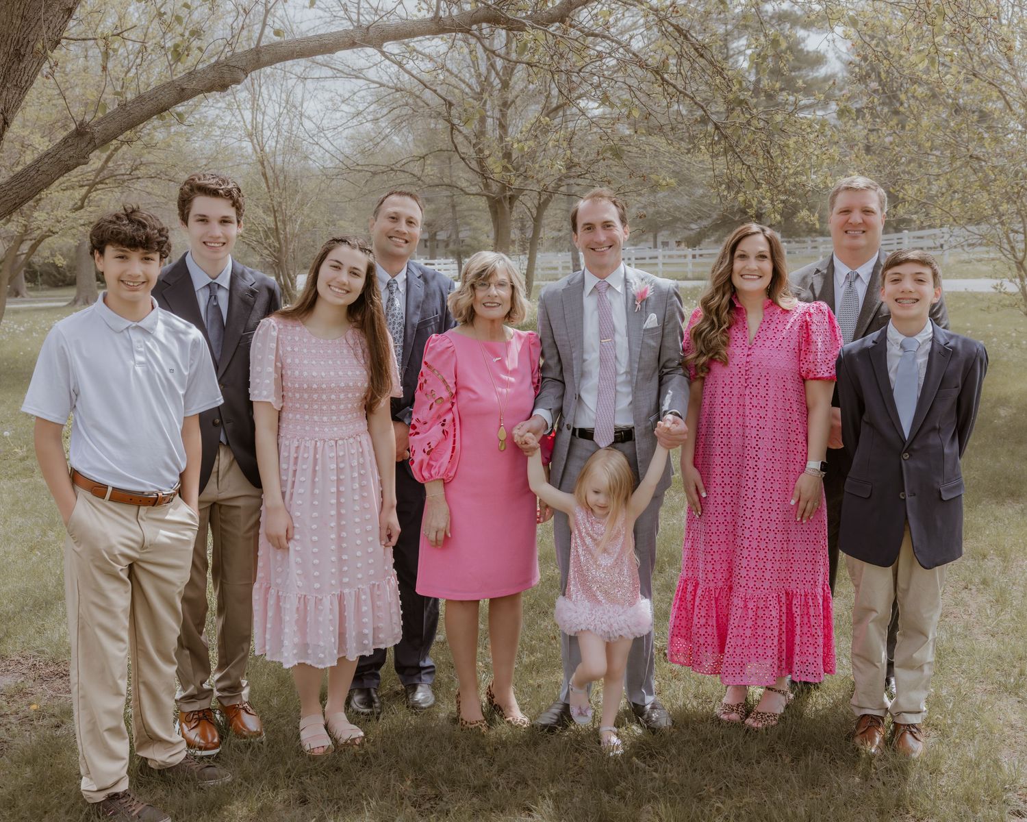 Large family group poses together outdoors in spring attire under blooming trees at celebration.