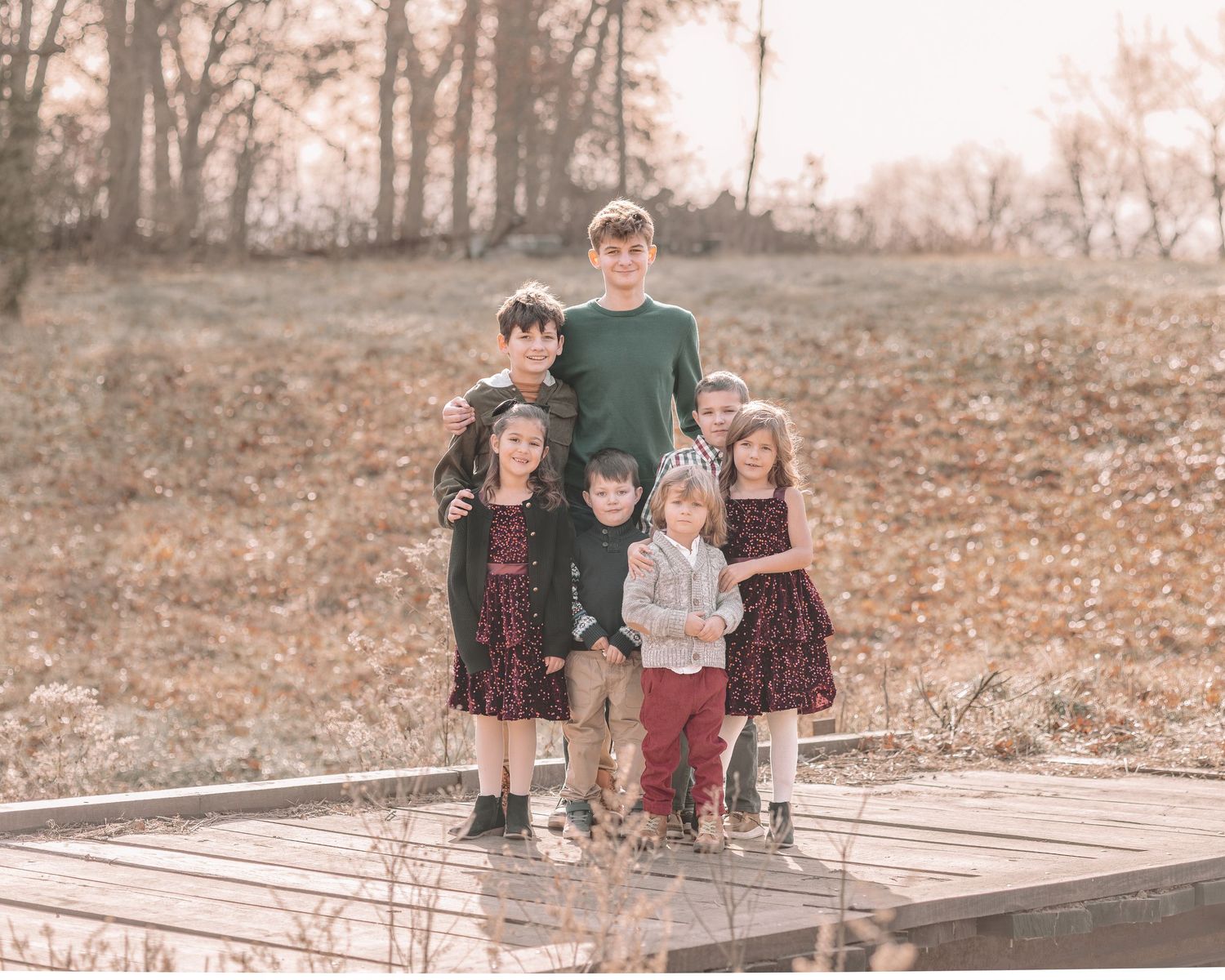 Family group poses on wooden deck surrounded by autumn trees and fallen leaves at sunset.