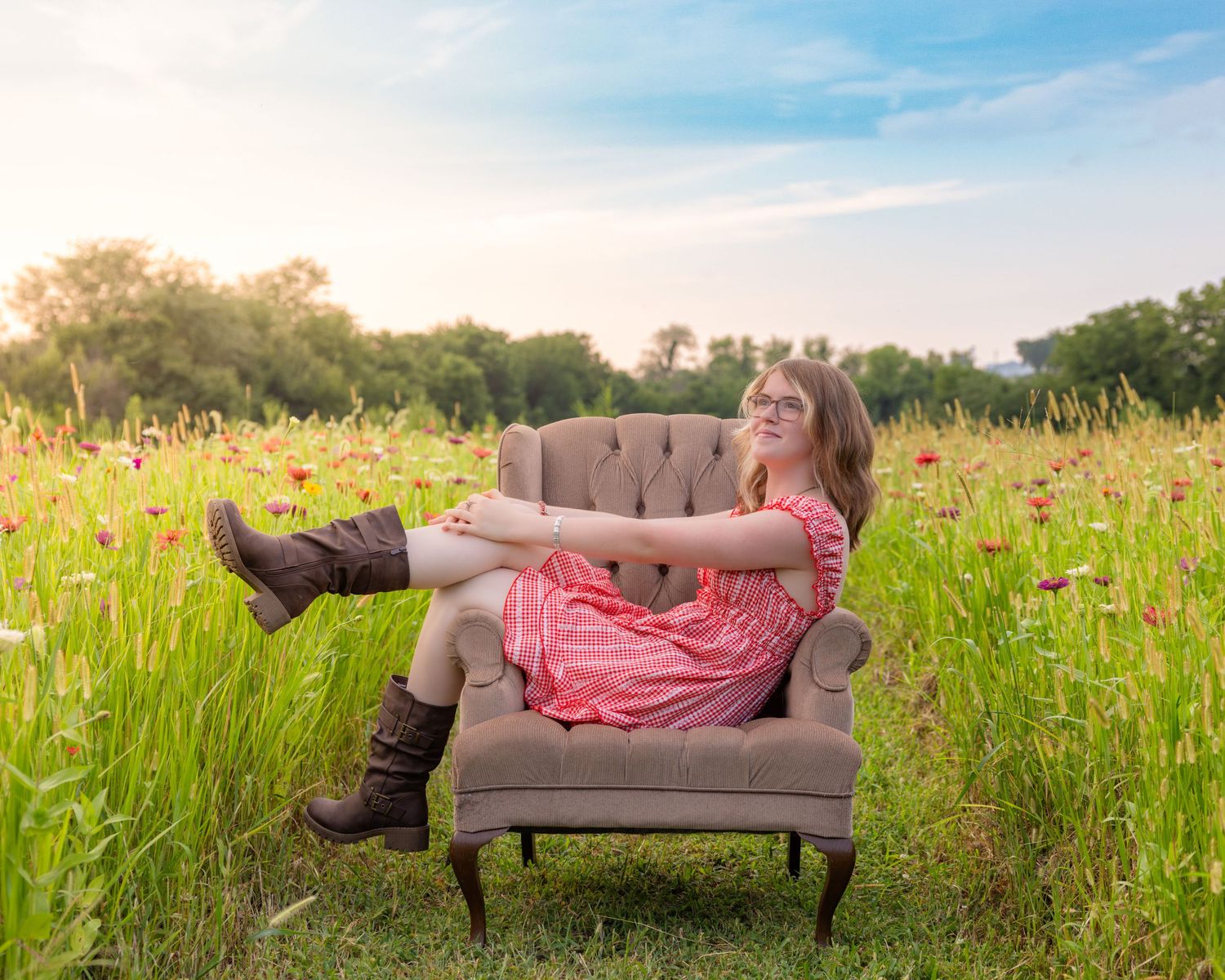 Young woman in pink dress and brown boots relaxing in armchair in a vibrant wildflower meadow at sunset.