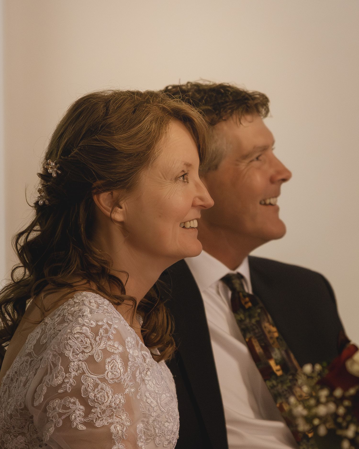 Smiling bride in lace dress and groom in suit with floral tie at wedding ceremony.