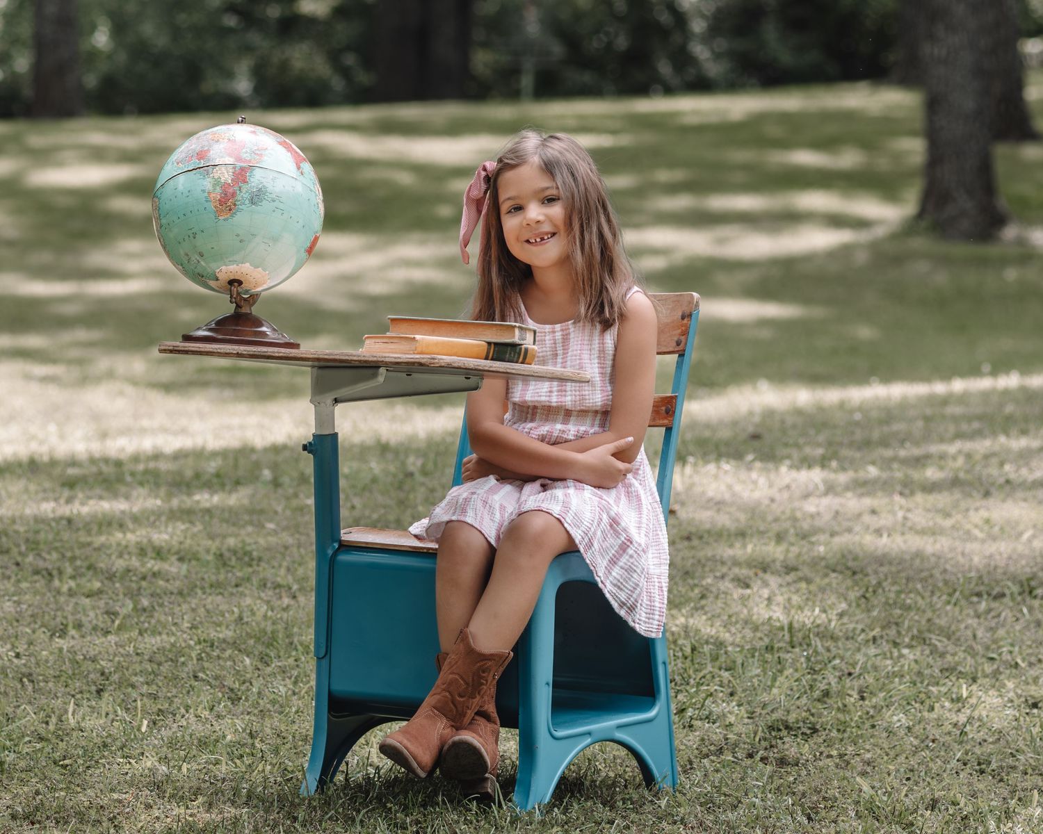 A child sits in a vintage turquoise chair outdoors on a sunny summer day in a park setting.