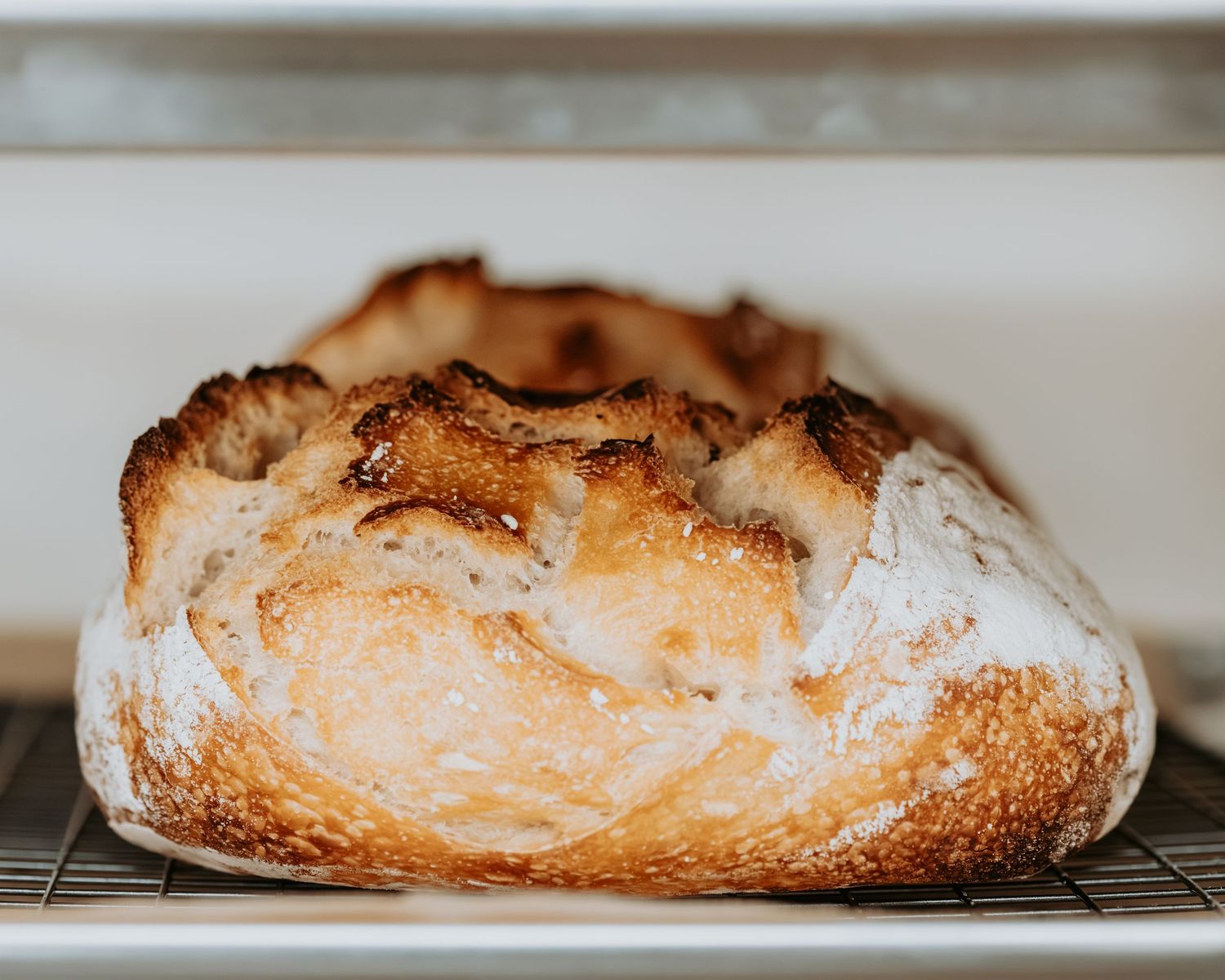 Freshly baked artisanal baguette with golden crust and rustic scoring marks displayed on a light surface.