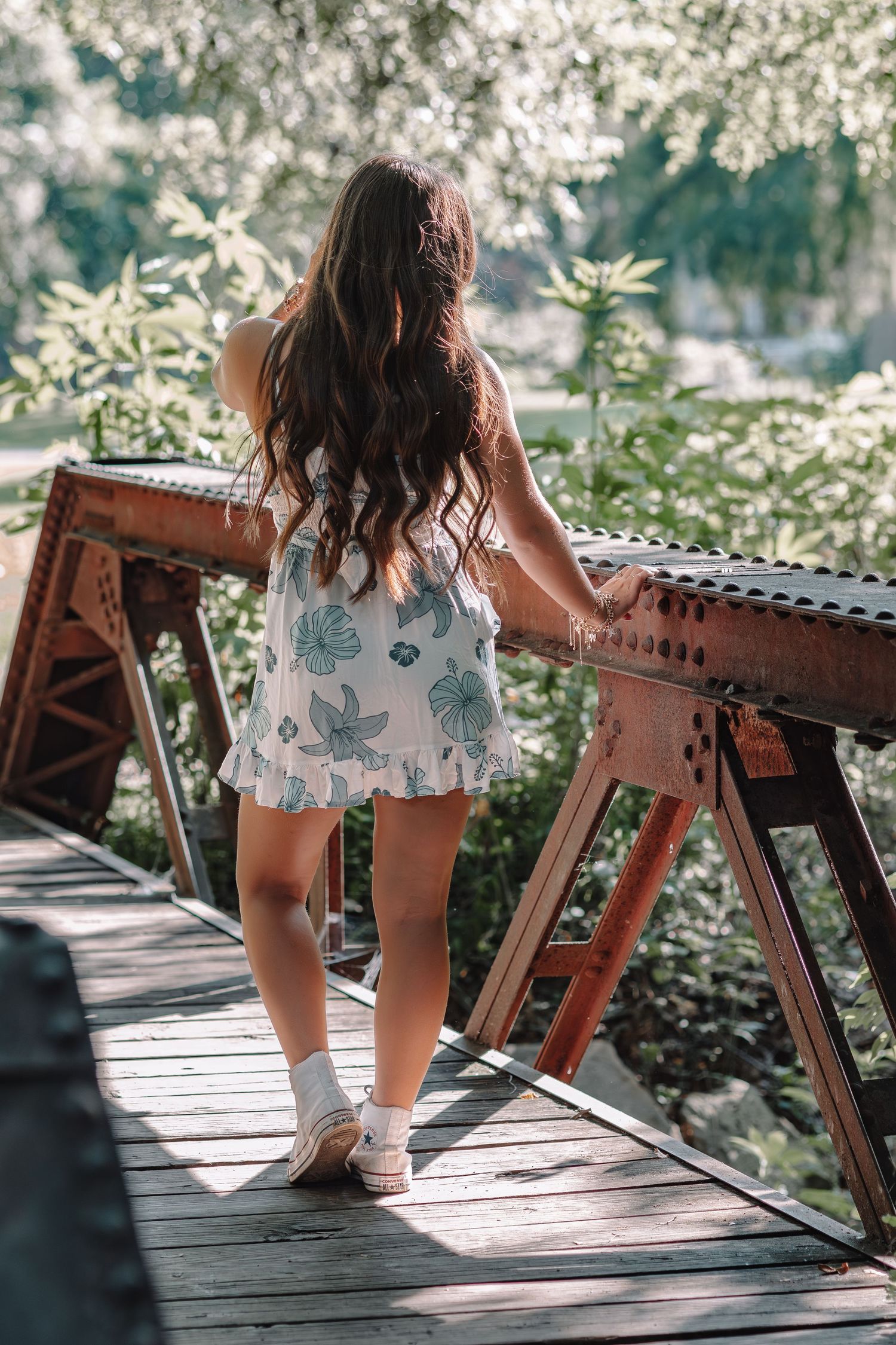 Person in a floral dress sitting on a rustic wooden bridge structure.