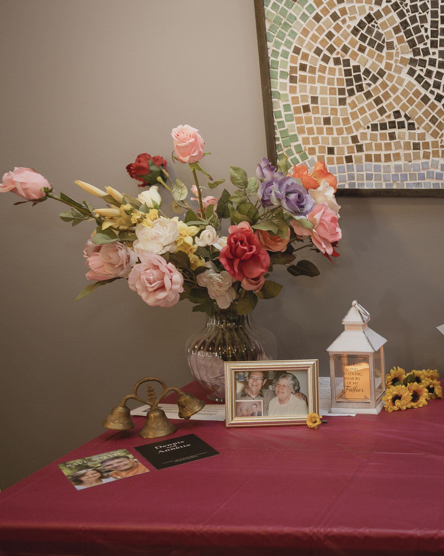Wedding reception table decorated with pink roses, white lanterns and mosaic wall art in the background.