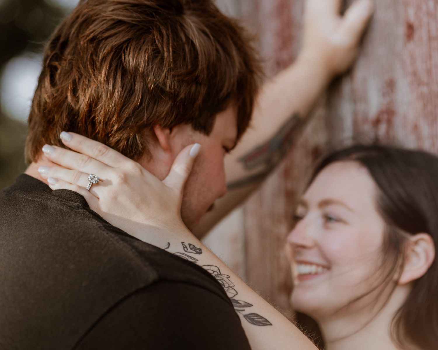 A smiling woman with tattoos tenderly holds a mans neck during a romantic couples engagement photo session.