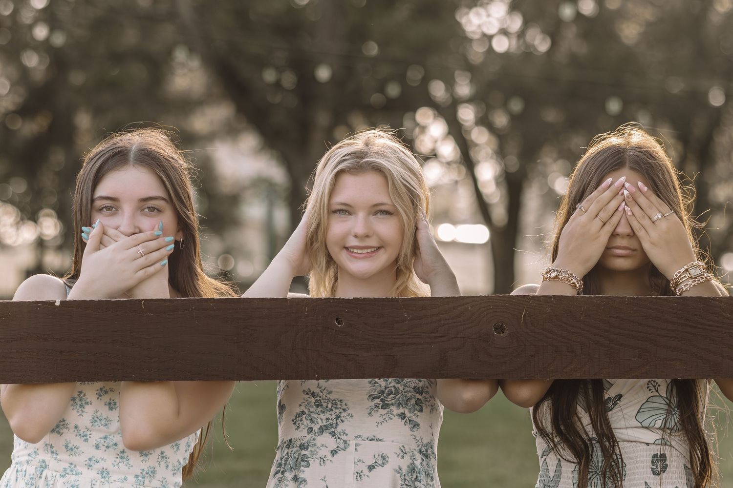 A group of people outdoors covering their eyes and faces with their hands in a playful manner.