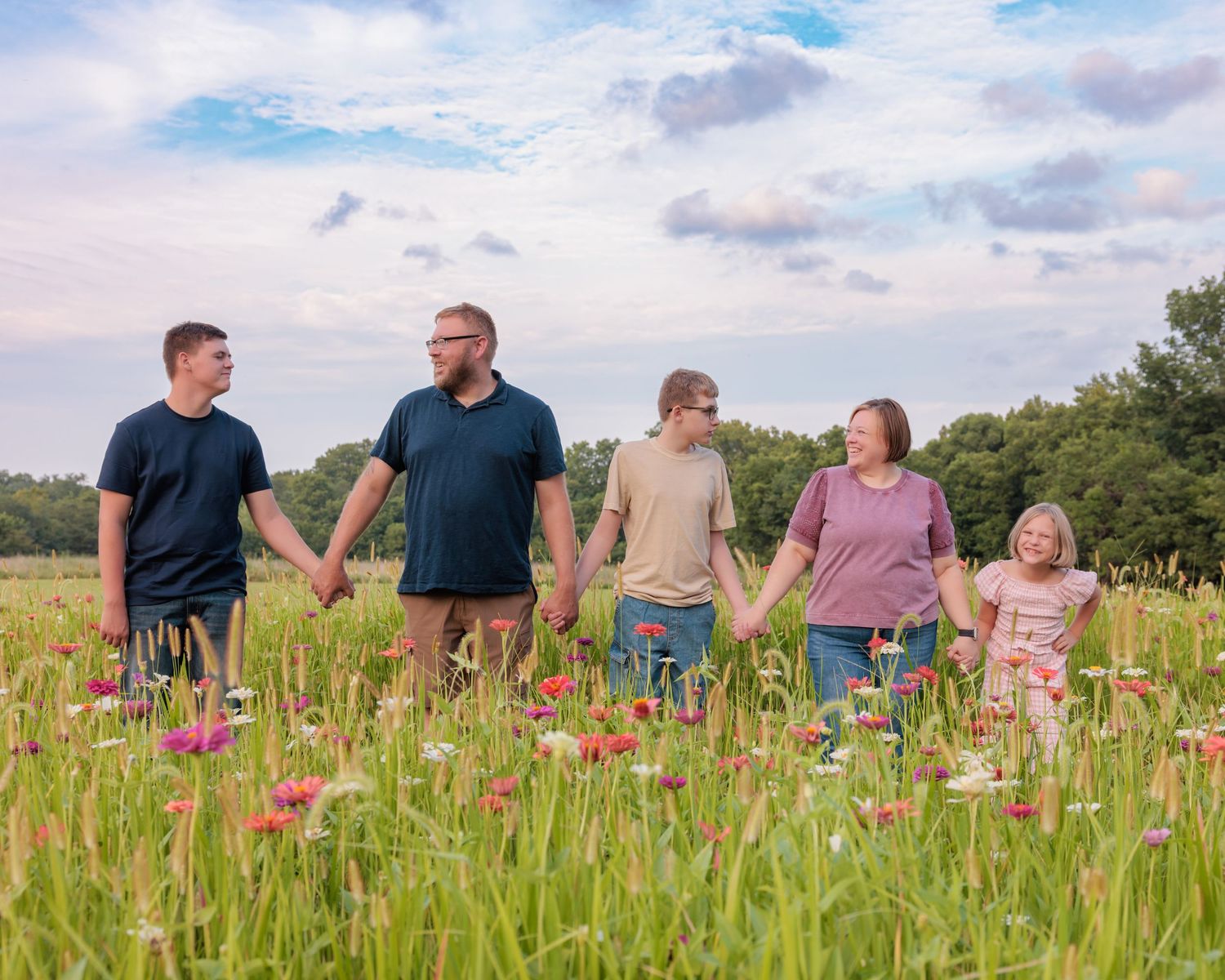 Five family members hold hands in a vibrant wildflower meadow under a cloudy sky.