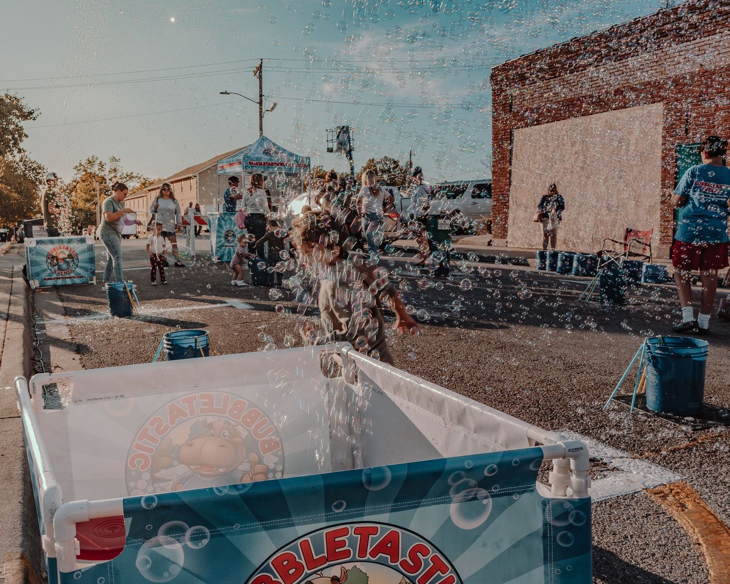 Panoramic view of a bustling street festival with vendor booths and crowds during golden hour.