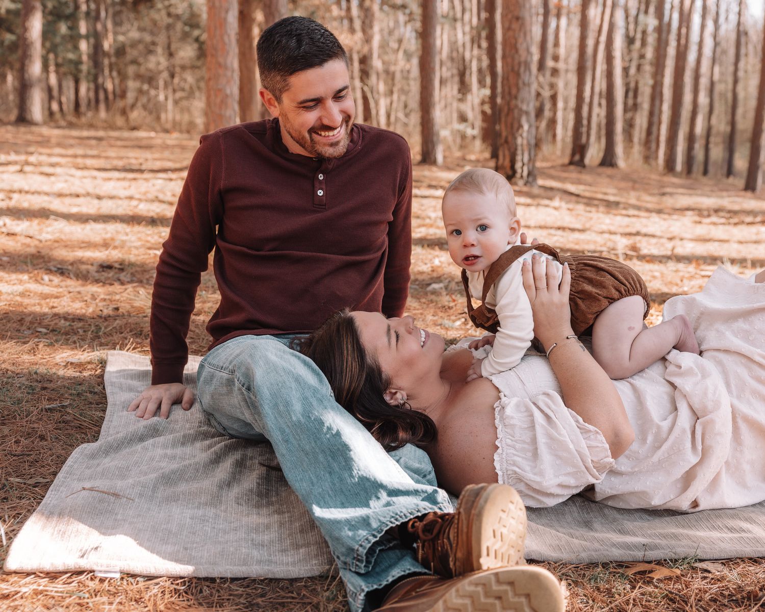 A heartwarming family moment captured on a blanket in a pine forest.