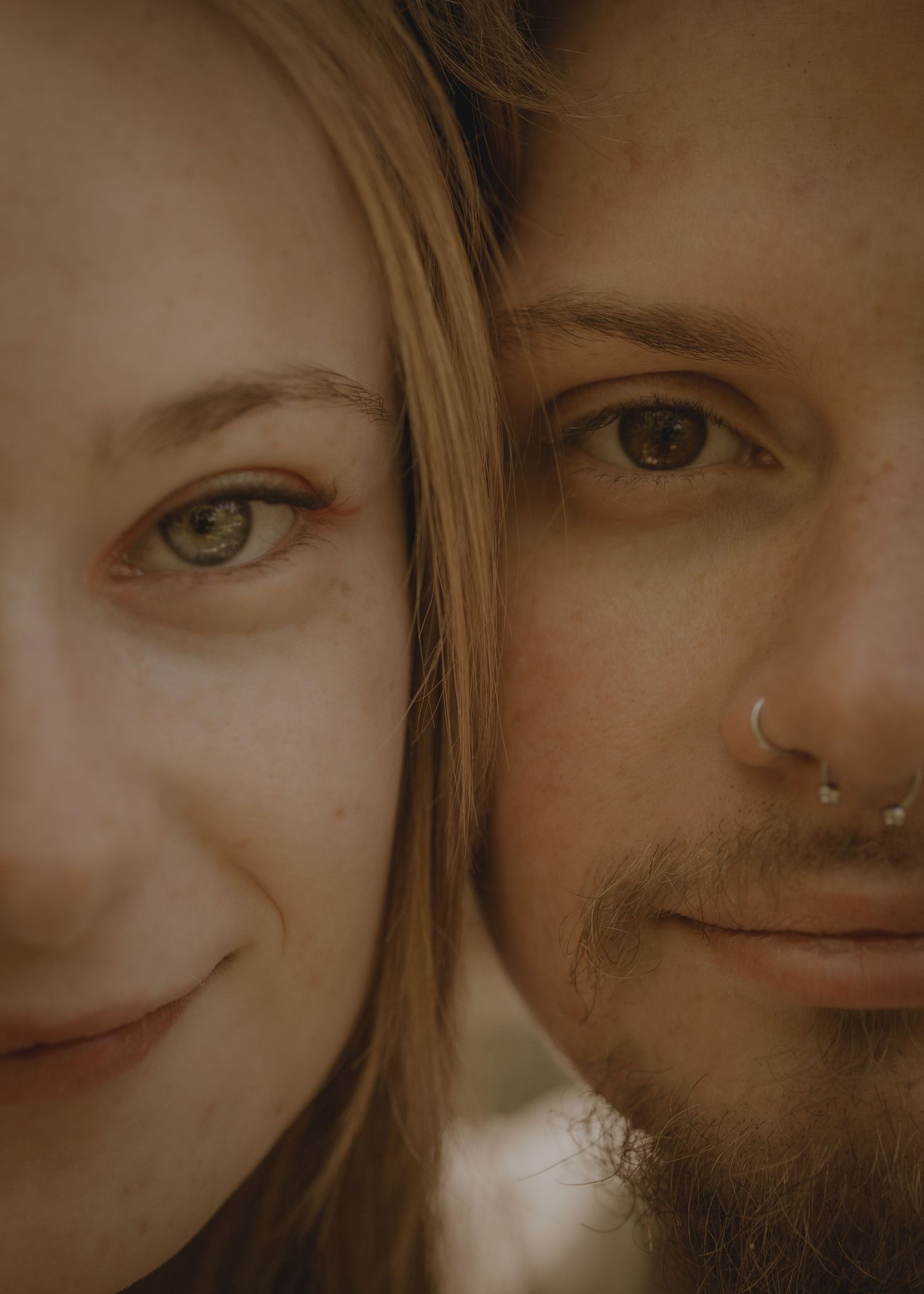 Close-up portrait of a woman with green eyes and a man with a nose ring, their faces side by side.