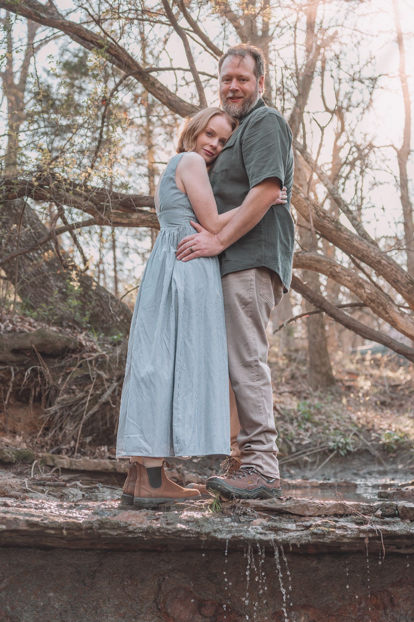 Couple embracing tenderly on a mossy surface surrounded by autumn trees.