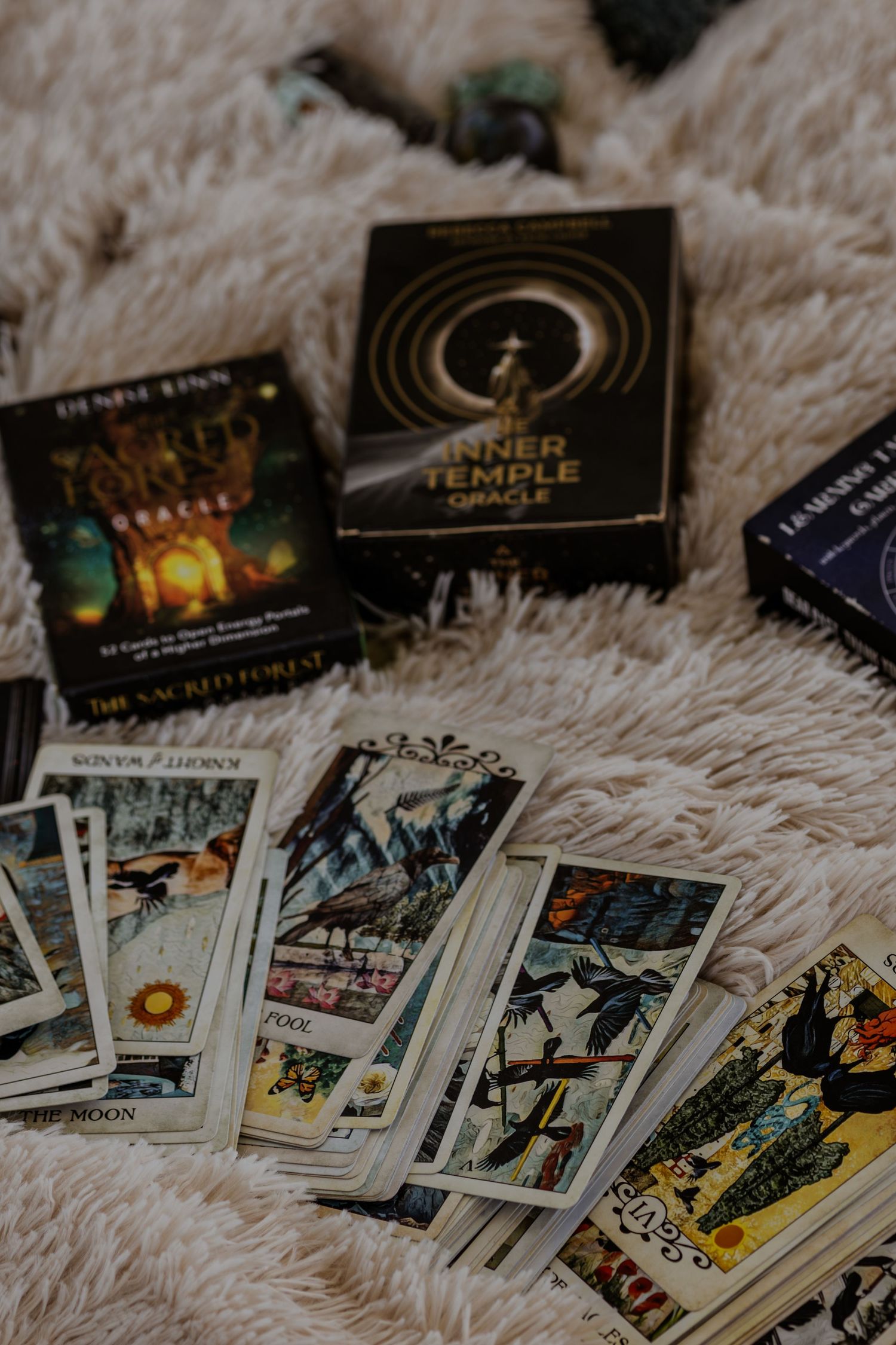 Tarot cards and mystical books spread out on a soft textured surface in moody lighting.