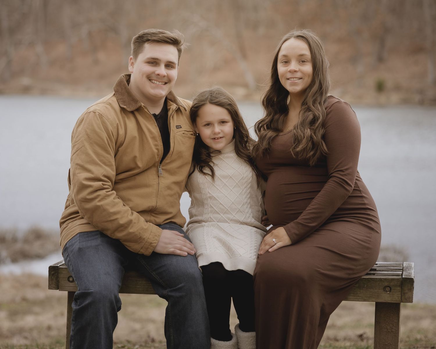 A family sits together on a wooden bench outdoors during an autumn photoshoot in warm earth-toned clothing.