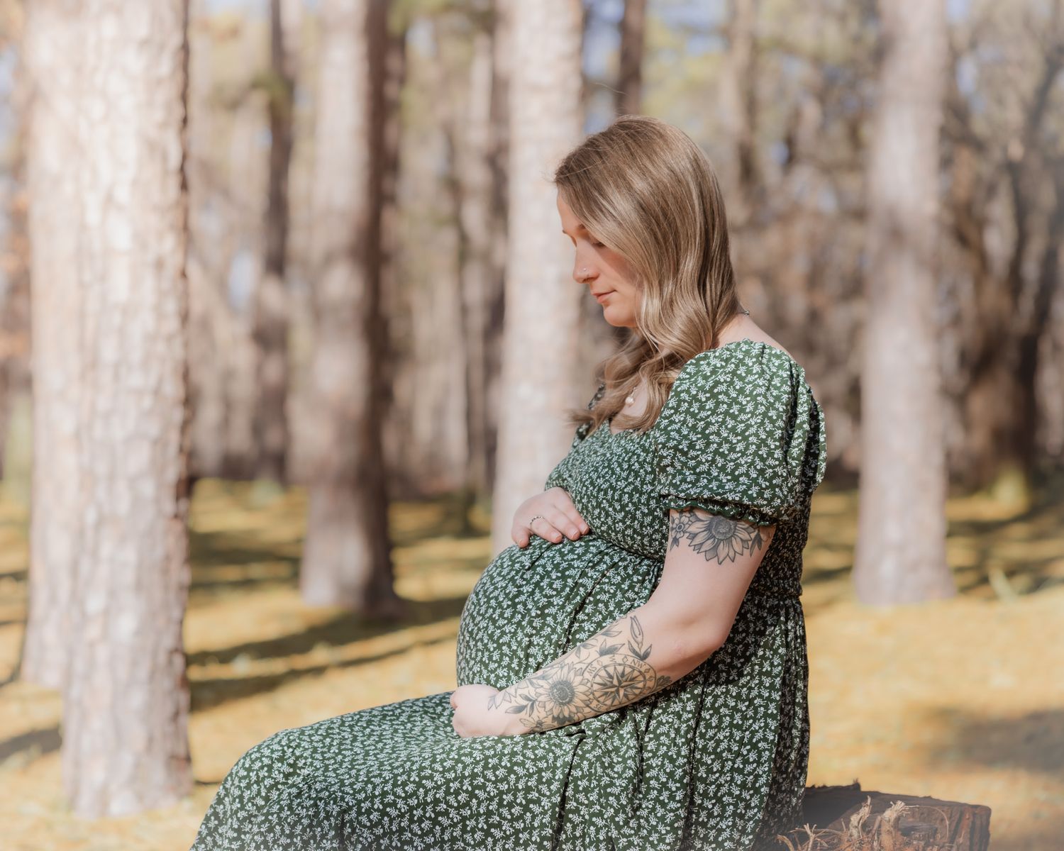 A woman in a green polka dot dress poses gracefully on a wooden bench in a sunlit forest setting.