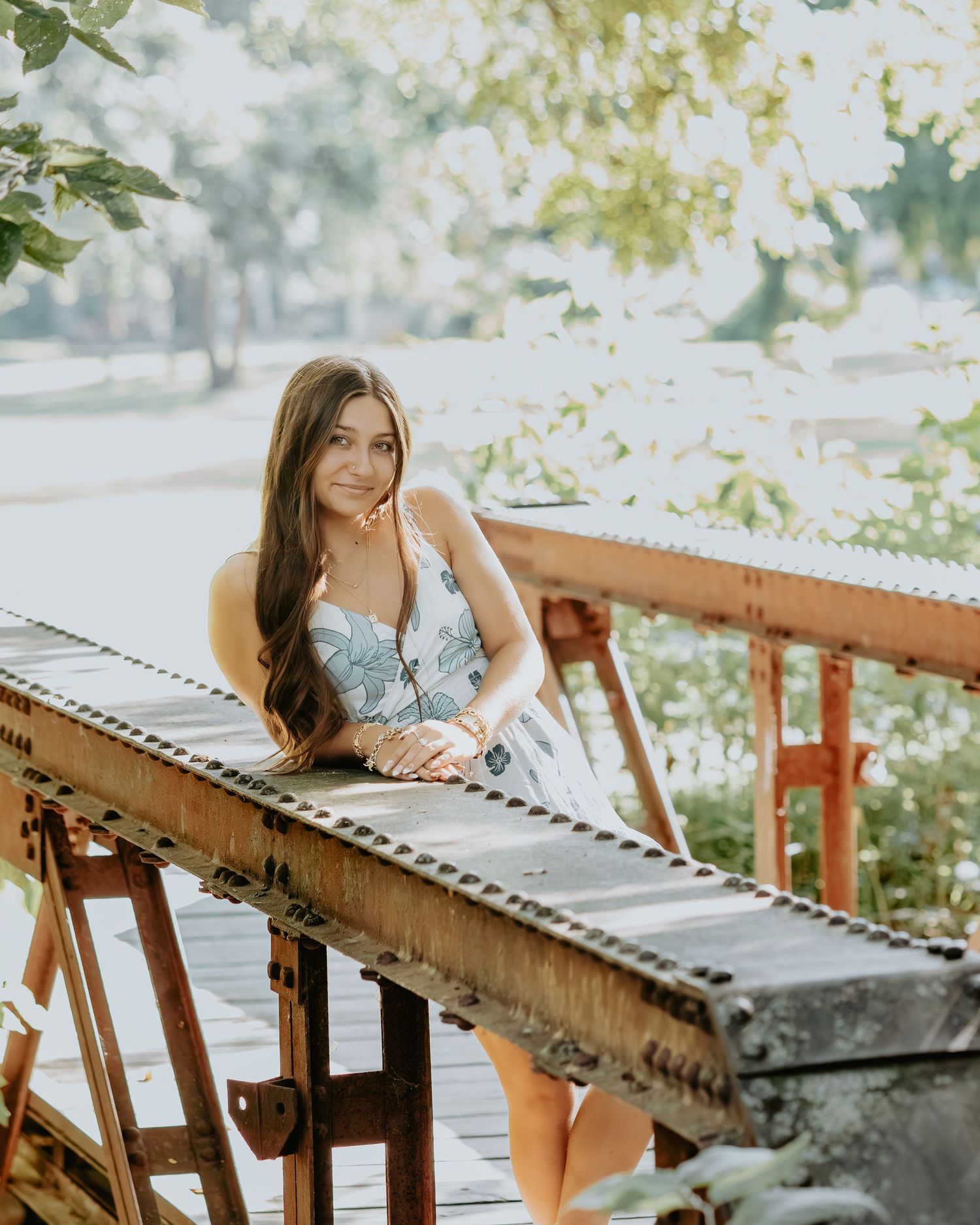 A woman in a floral dress leans against an industrial conveyor belt in a natural outdoor setting.