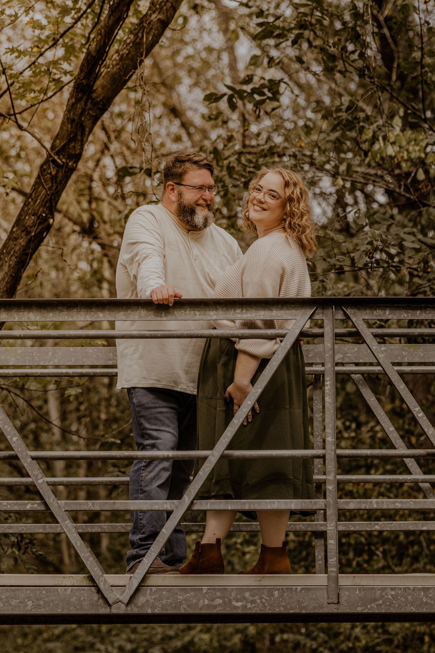 A couple shares a romantic moment on a rustic wooden bridge surrounded by autumn foliage.