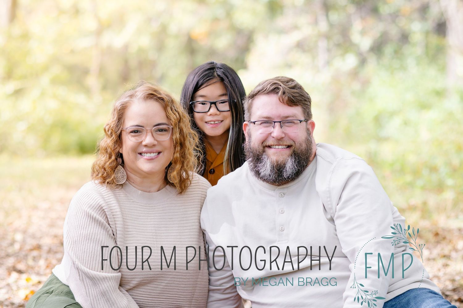 A family in casual attire sits together outdoors during a fall photo session with natural lighting and autumn colors.