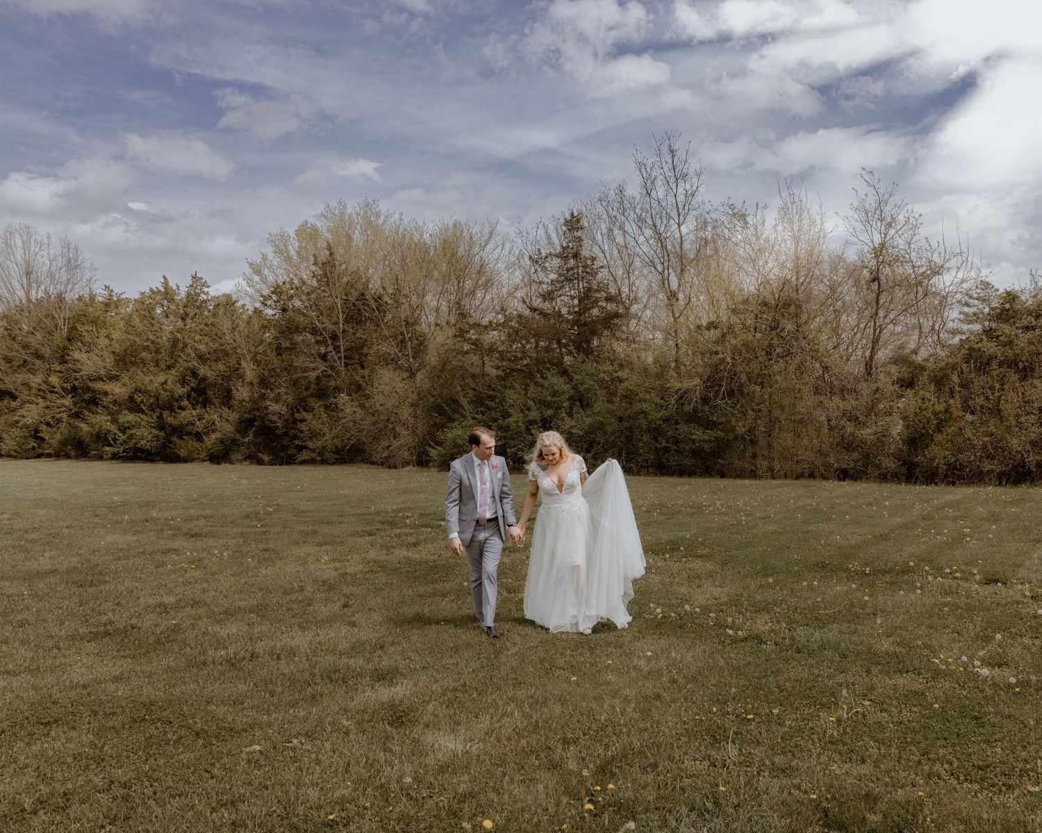 Bride and groom walking hand in hand across a green field on their wedding day.