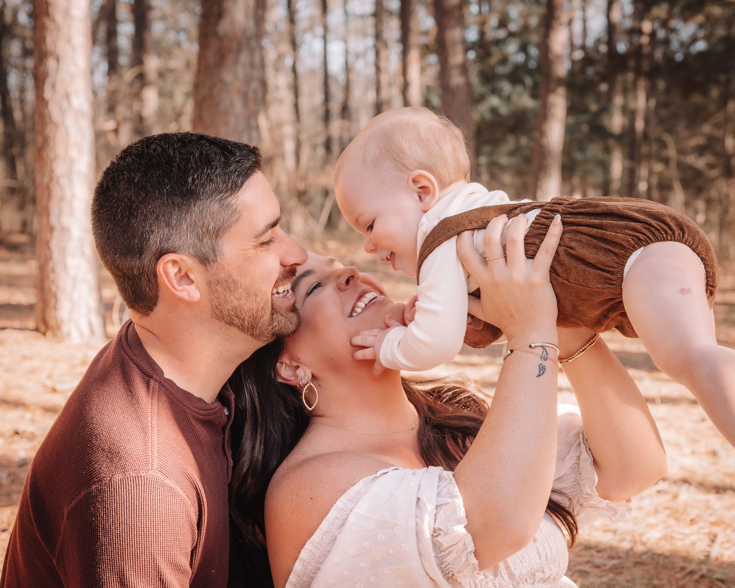 A candid family photoshoot showing playful moments in a sunlit forest setting.