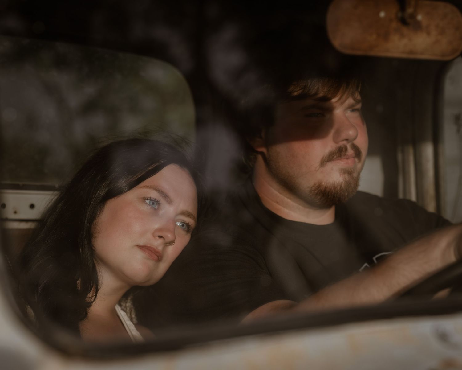 A young couple sits inside a vintage truck, the woman leaning on the man's shoulder in a moody, intimate portrait.