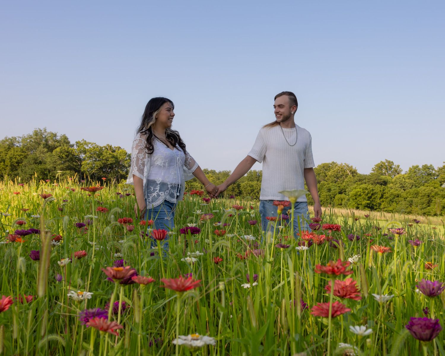 Couple holding hands in a vibrant wildflower field with colorful blooms under a clear blue sky.