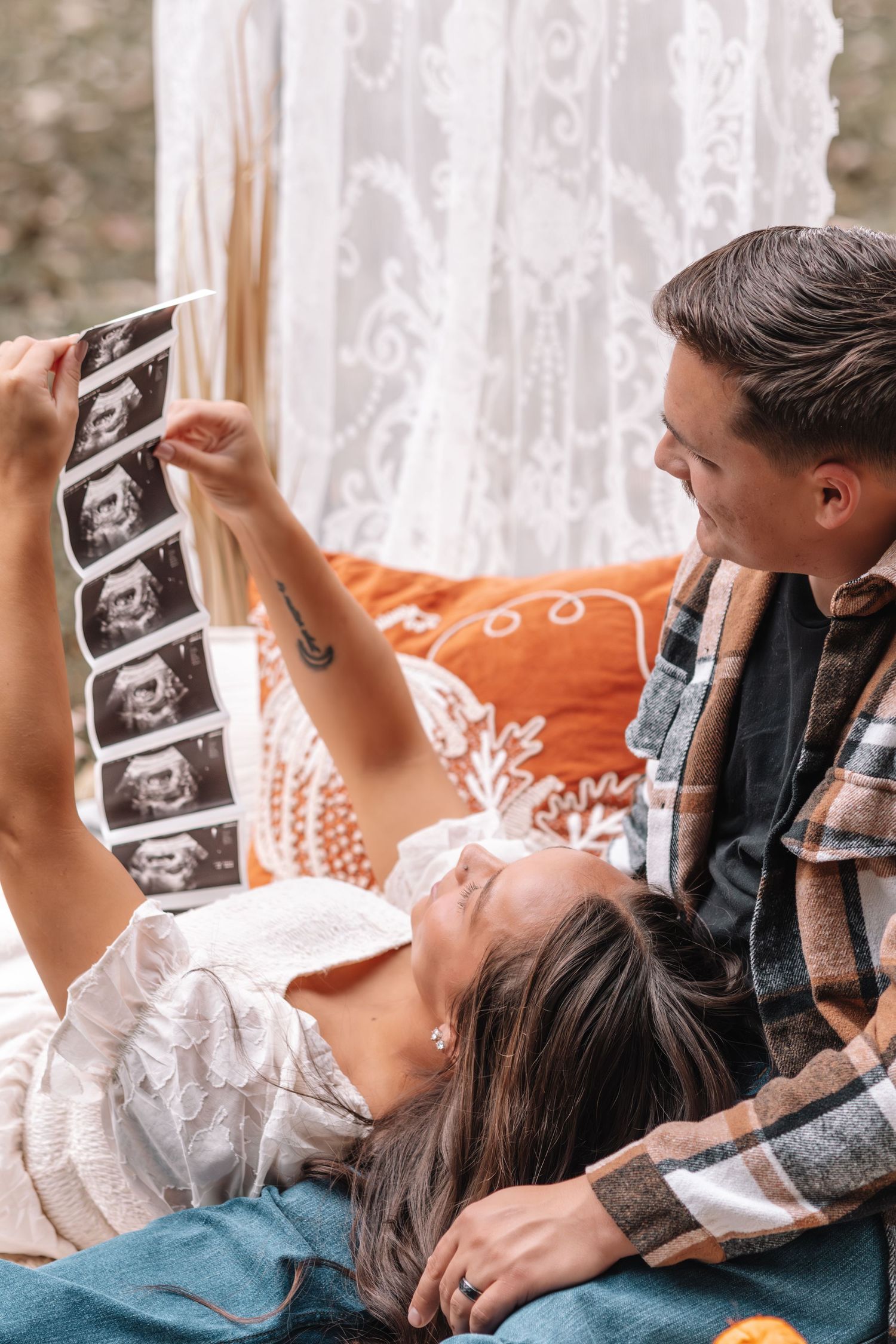 A couple lying down together looking at ultrasound photos in a cozy home setting.