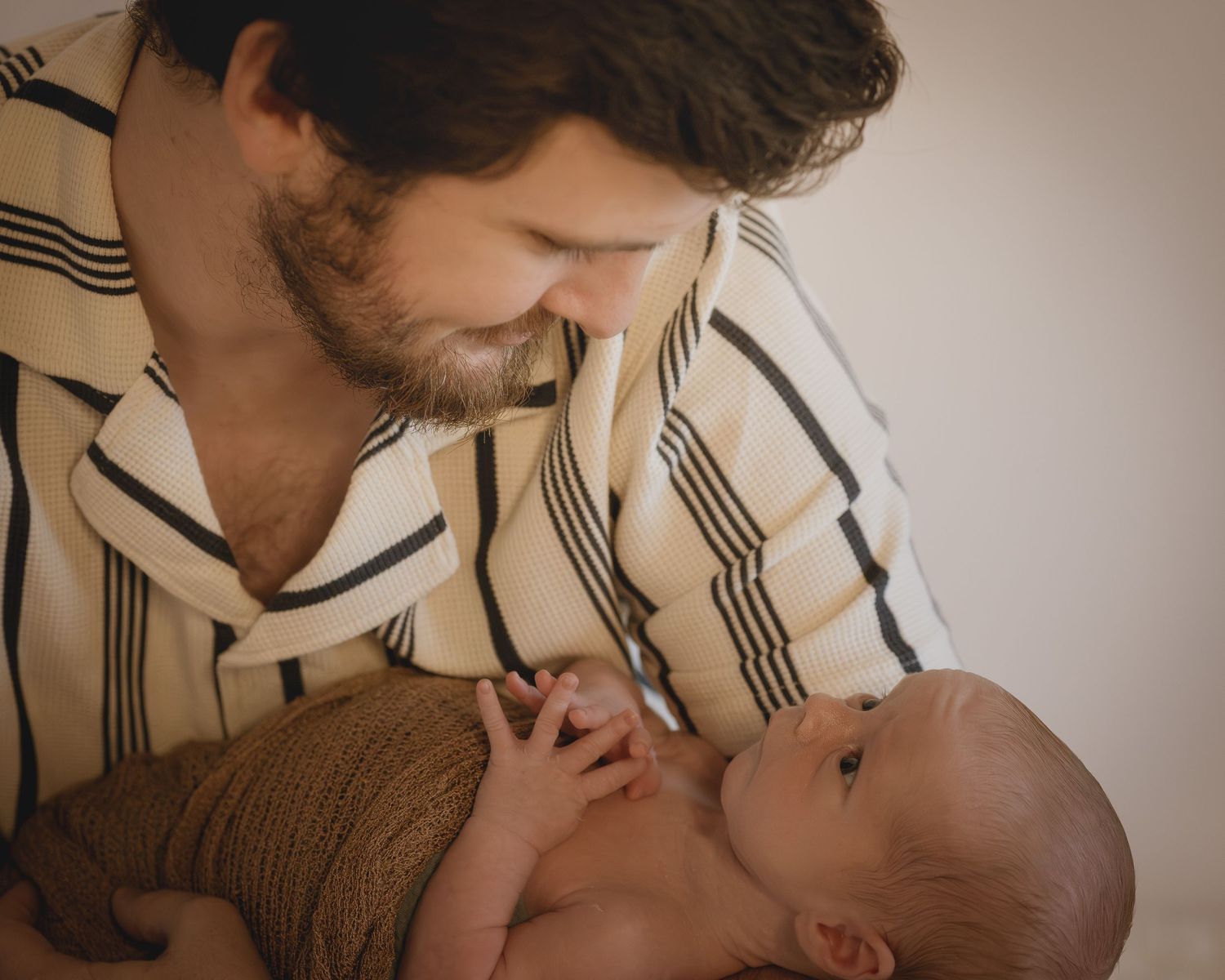 A bearded father gazes tenderly at his newborn baby wrapped in brown.