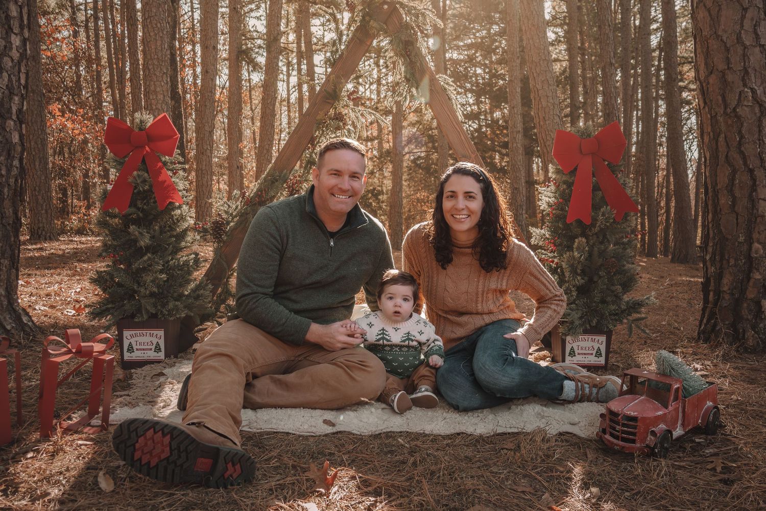 Family sitting together with their dog on blankets in a scenic autumn forest with red and orange foliage.