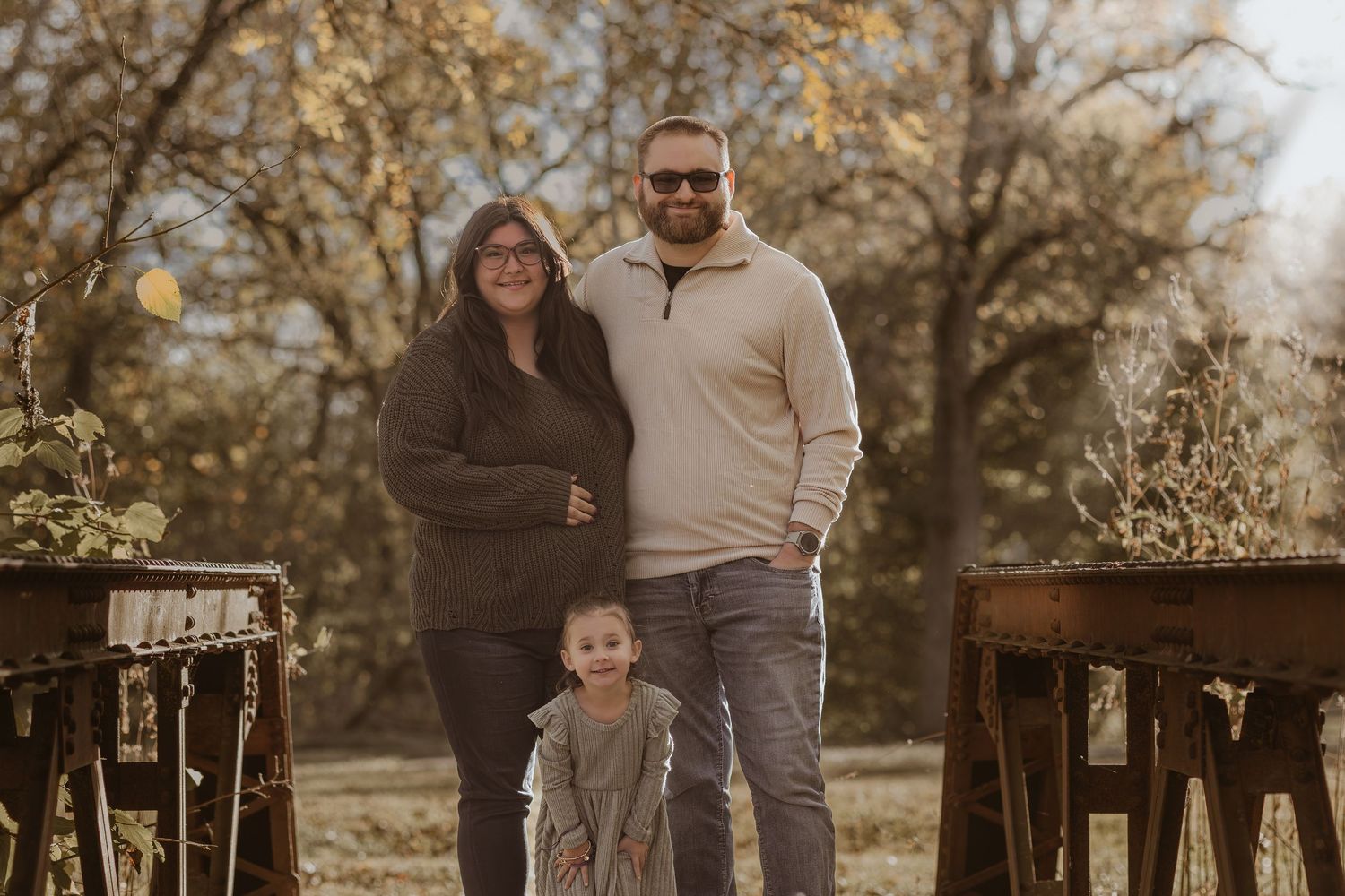 Group portrait in casual attire standing together on wooden walkway during golden hour.